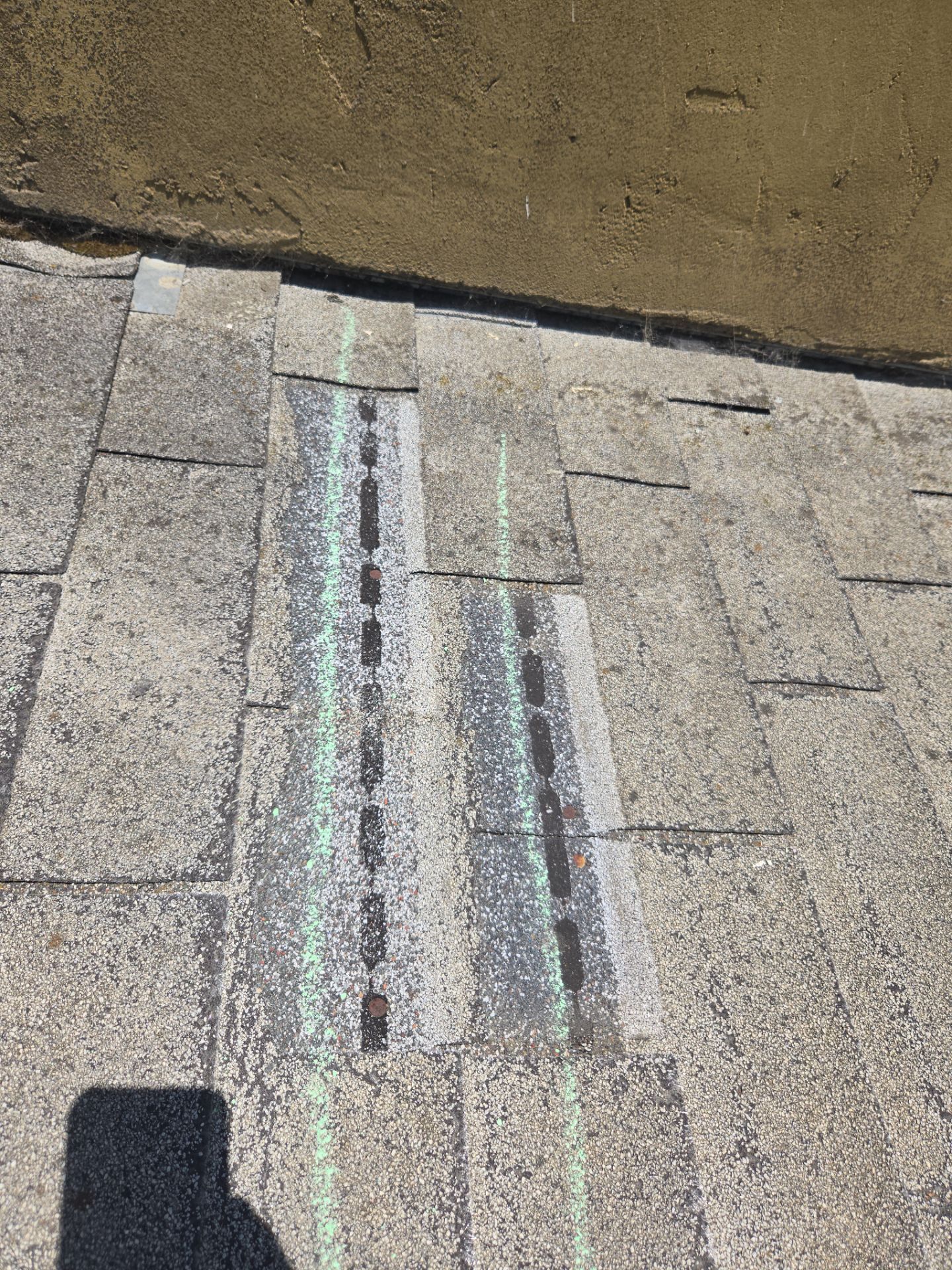 Close-up of shingles along a stucco wall with parallel chalk-marked repair strips