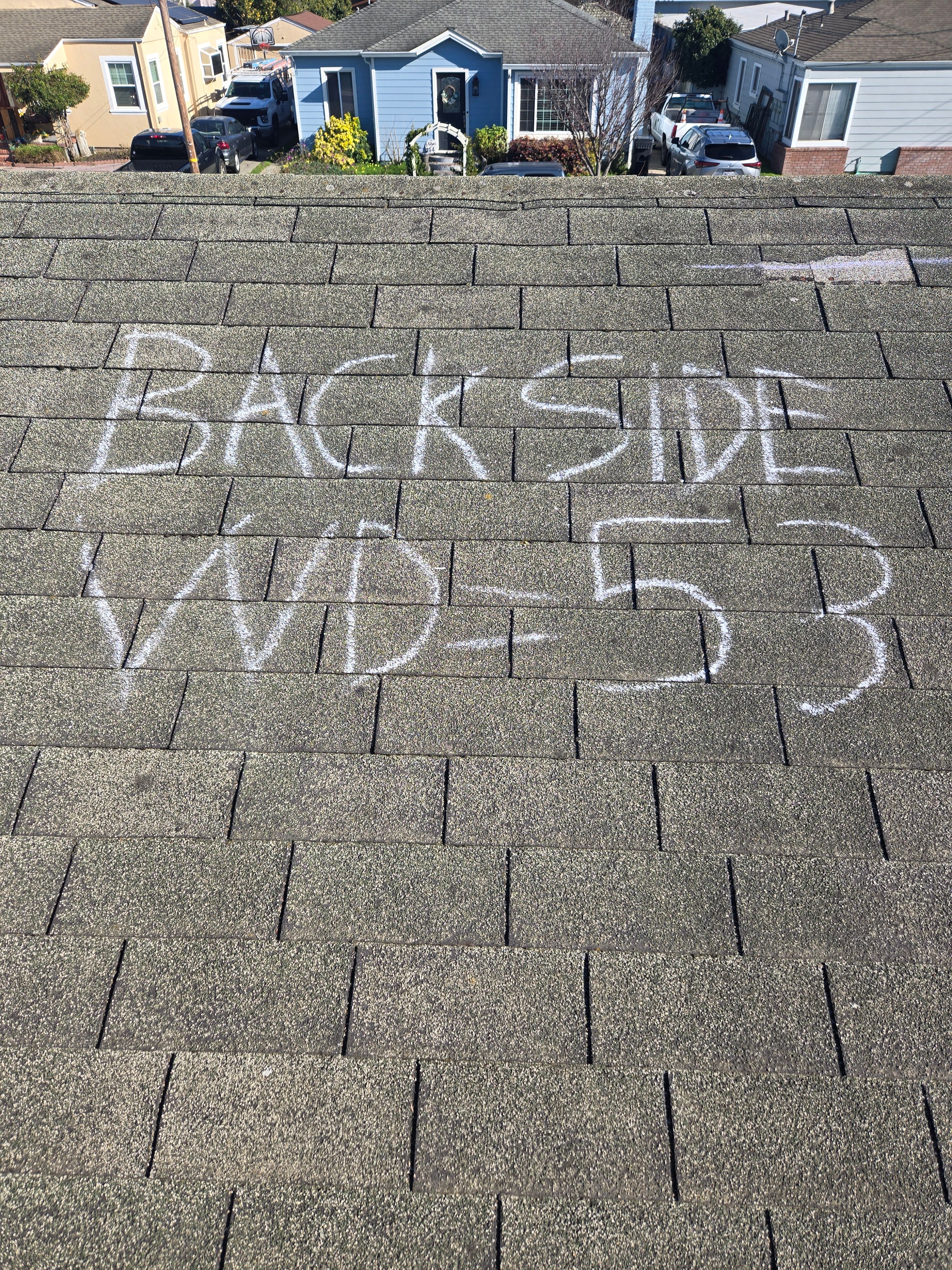 Chalk-marked wind damage labeled Back Side WD-53 documented during a roof inspection
