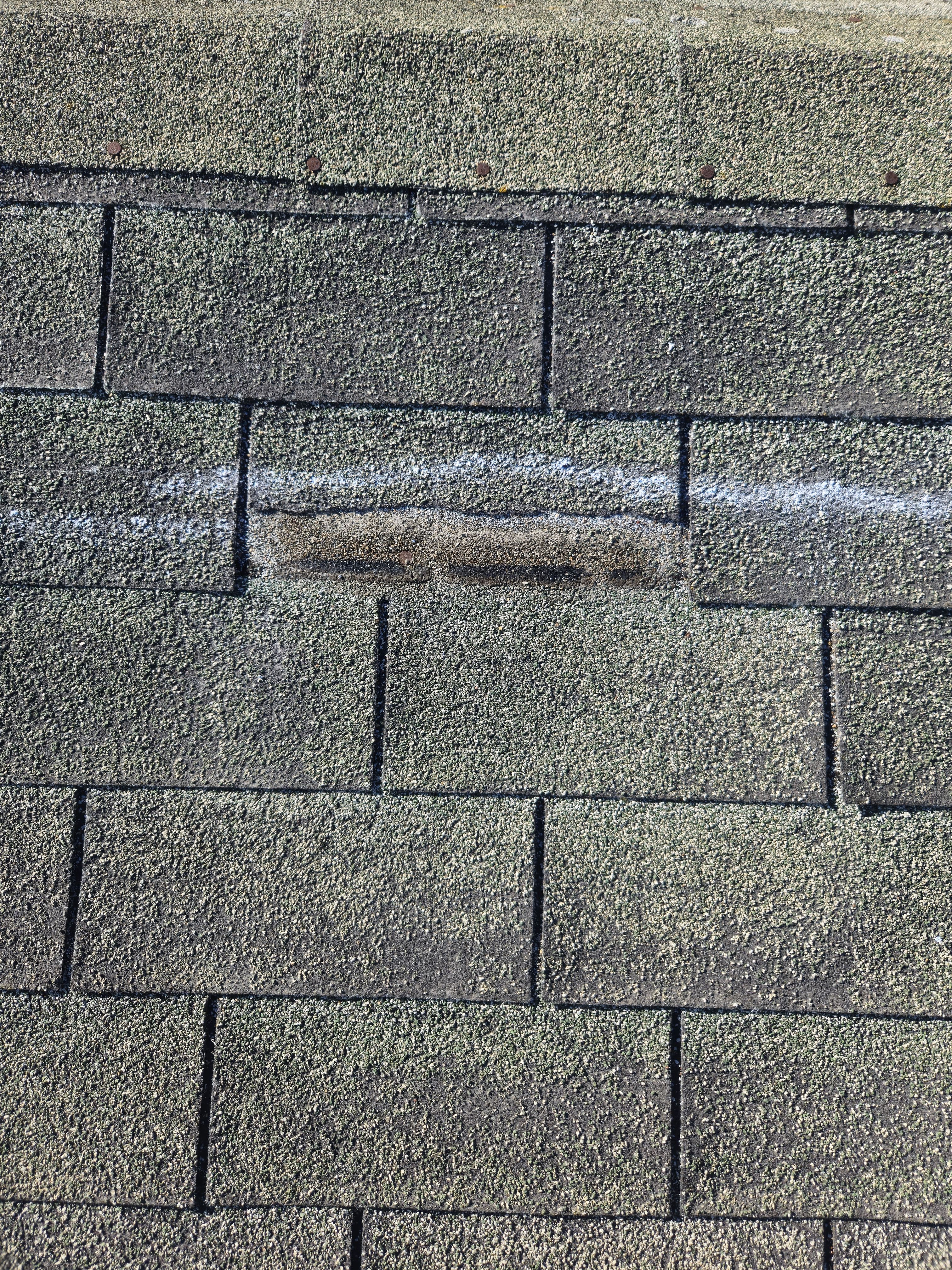 Close-up of a storm-damaged shingle marked during claim documentation